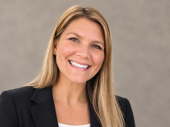 A blonde woman smiles in a black blazer and a white shirt.