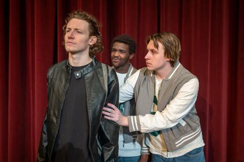 Three male students in letterman jackets pose on a stage.