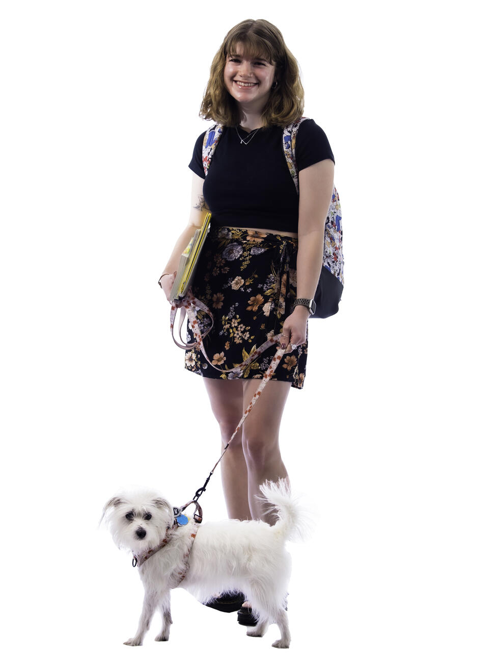Micaela Champion poses while holding a textbook and her small white dog on a leash.