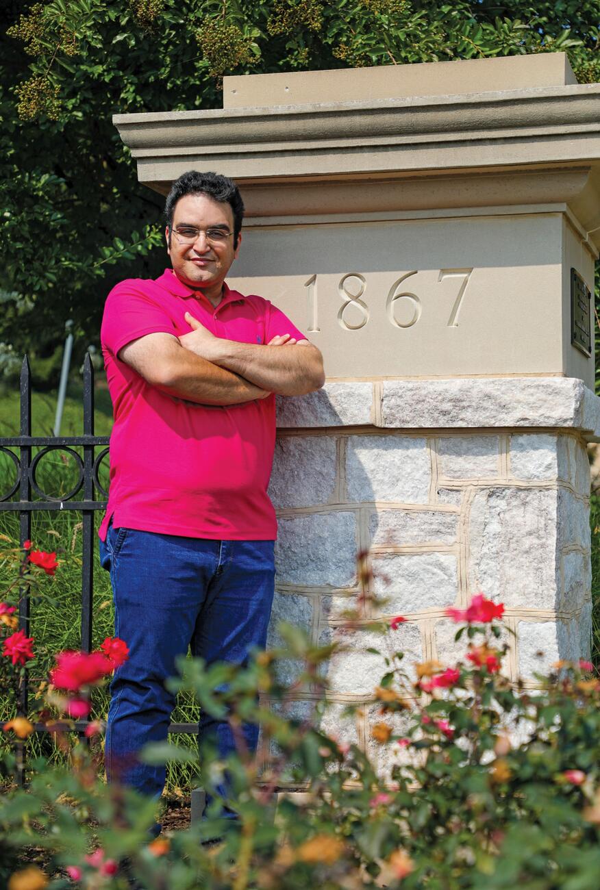 Photo of professor Farzad Ahmadi standing by a stone pillar on campus with 1867 inscribed on it.