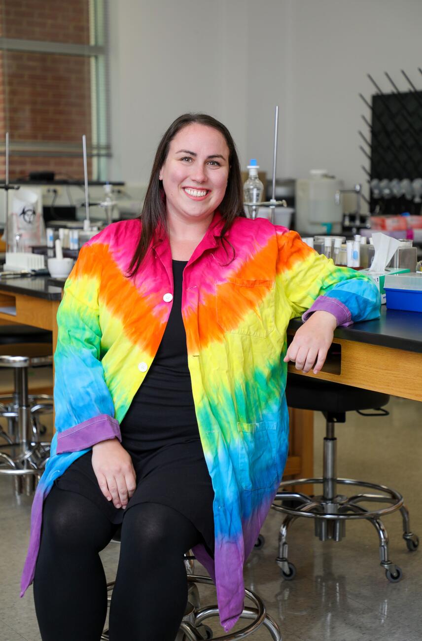 Photo of professor Maureen Williams in a tie-dyed lab coat sitting in a science lab.