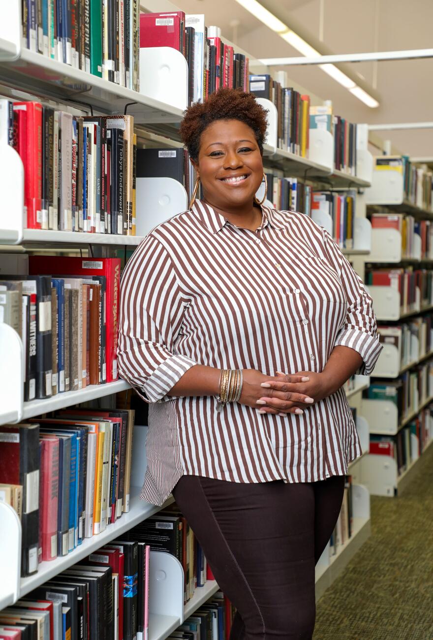 Photo of professor Shaeeda Mensah in front of a bookcase in the library.