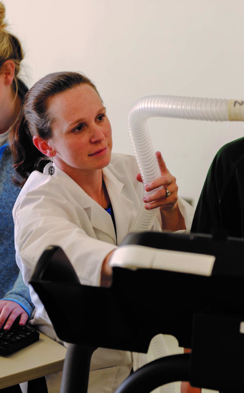 Photo of professor Jennifer McKenzie in a lab coat holding a breathing tube in the lab.