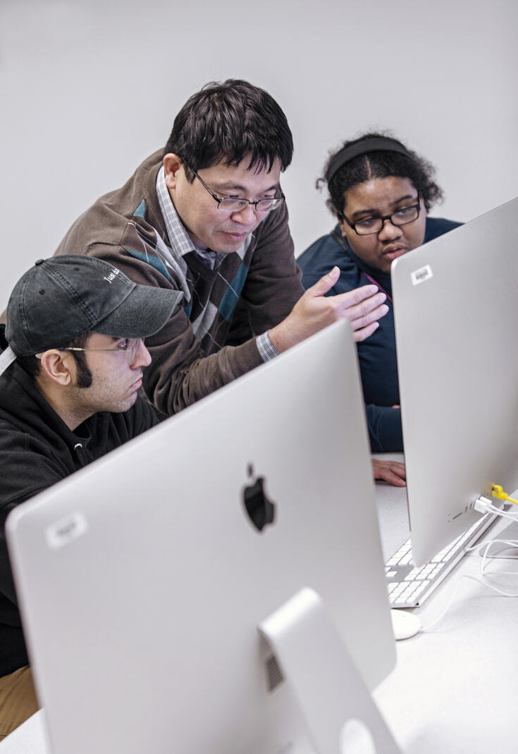 Photo of professor Paul Lin speaking with students at a computer.