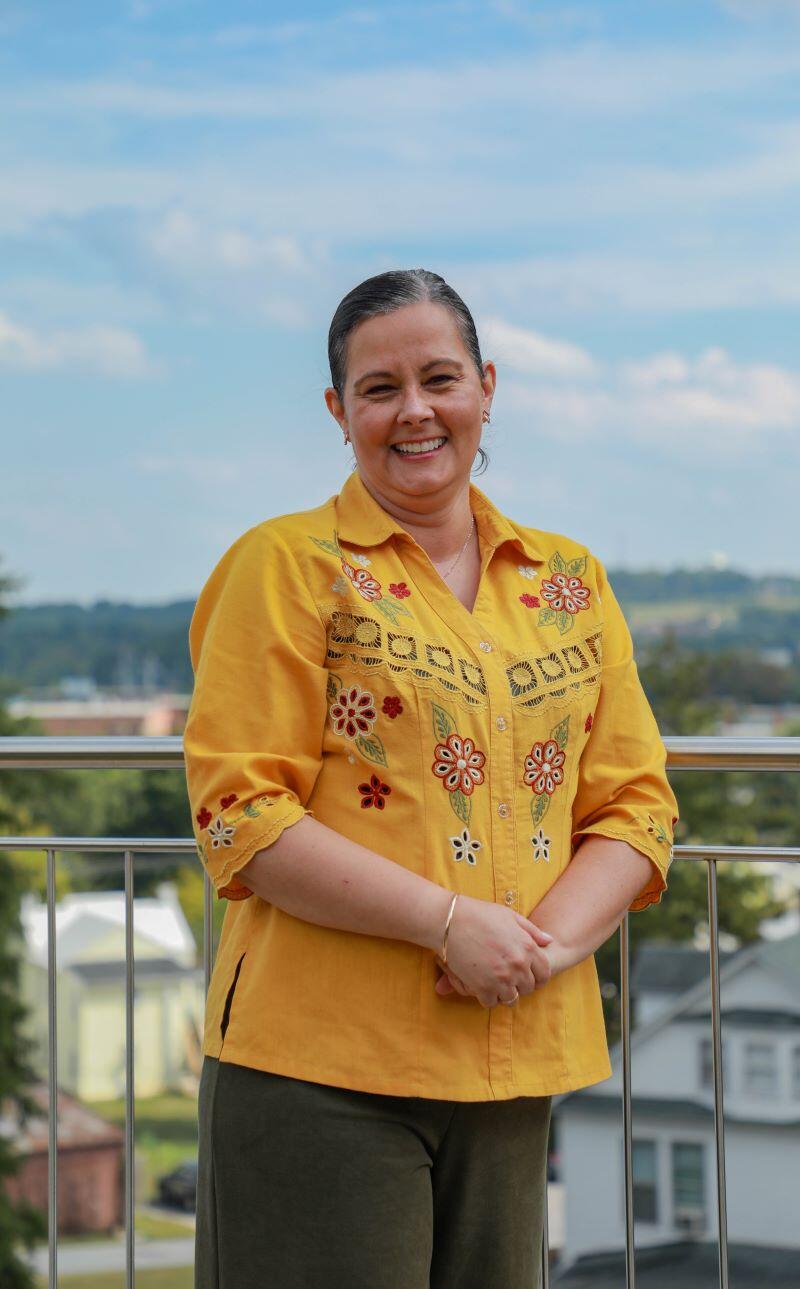 Photo of a woman standing on an overlook wearing a yellow flowered shirt with horizon behind her.