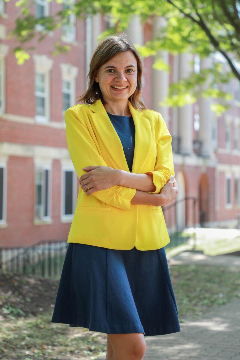 Photo of a white female in a bright yellow suit jacket standing in front of a brick academic building.