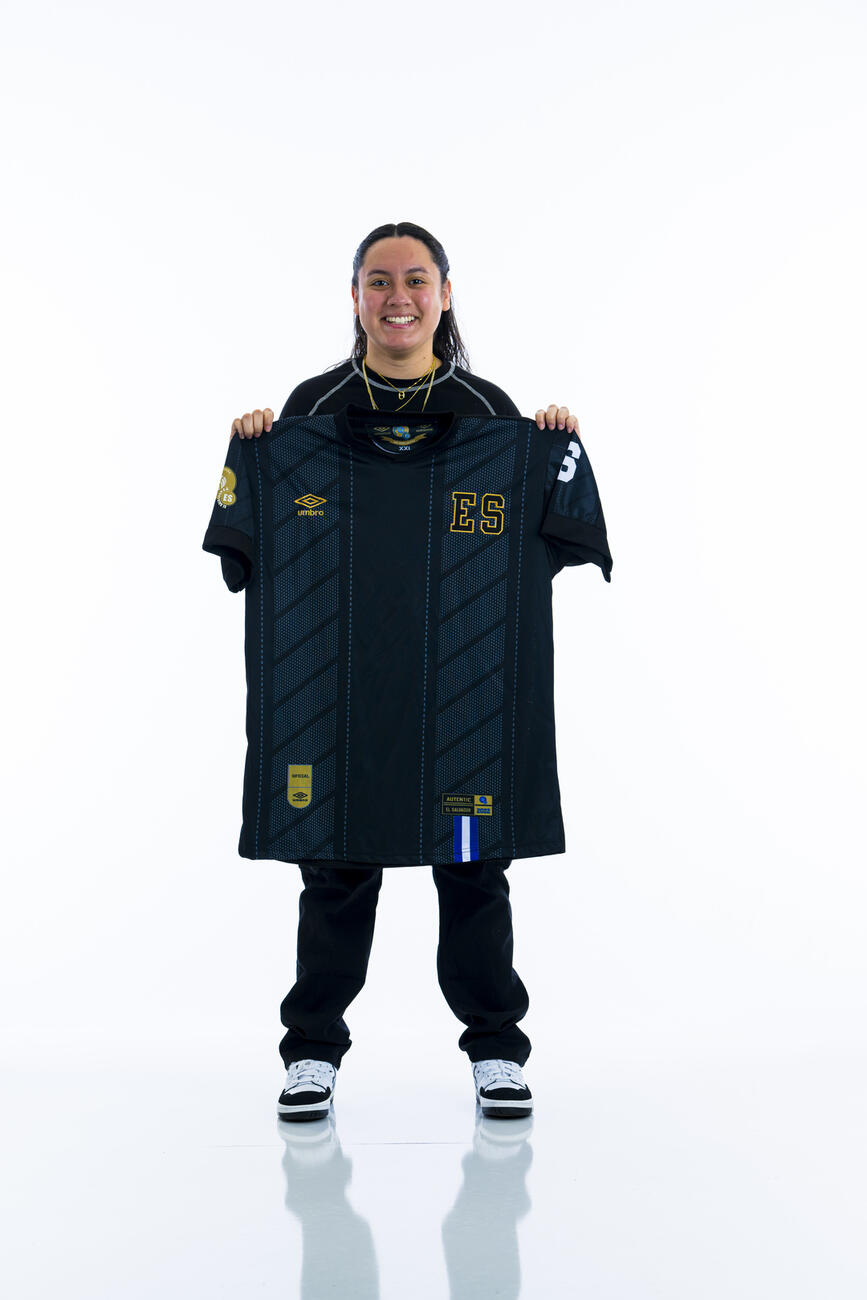 A student holds out an El Salvador jersey in front of a white background.