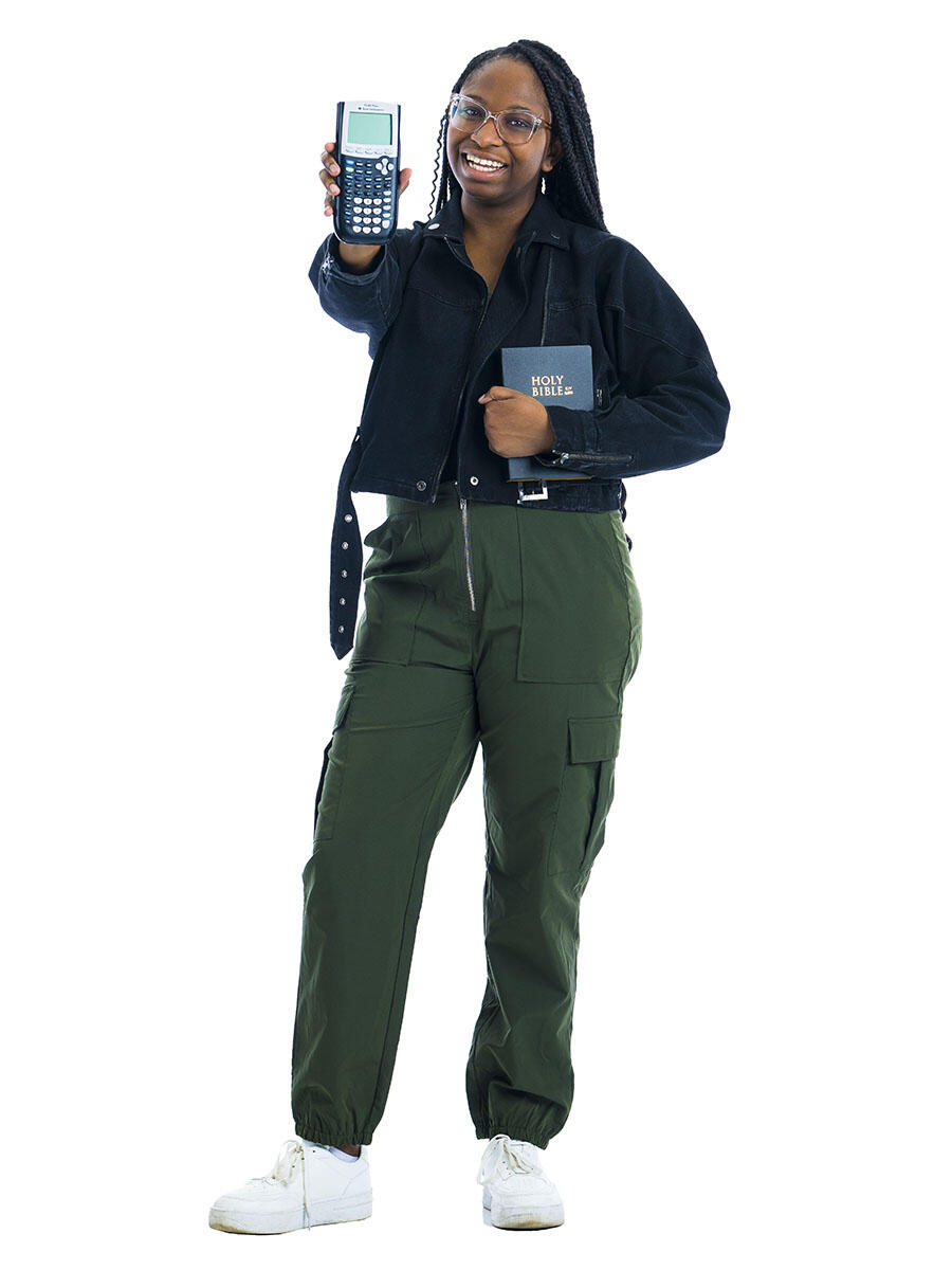 A student holding a Bible and a calculator stands in front of a white background.