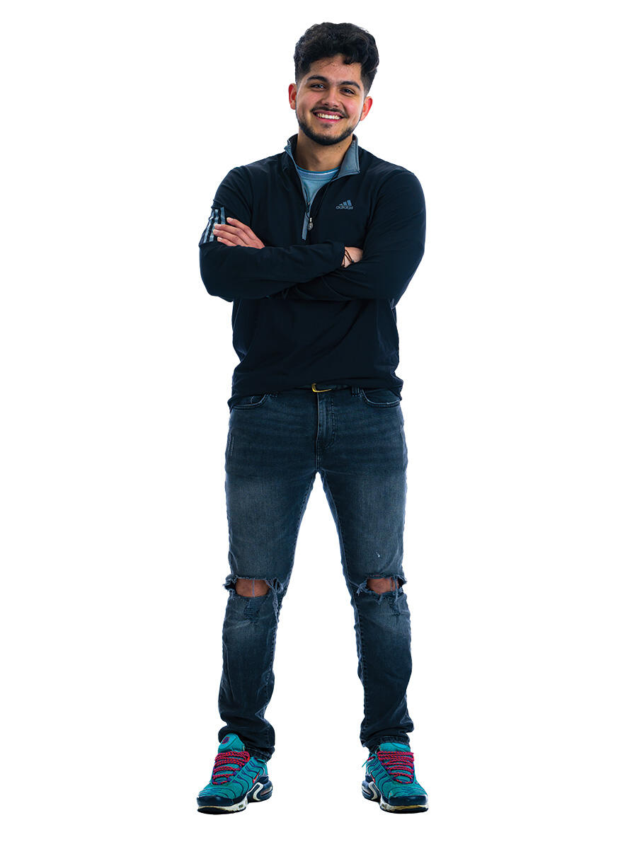 A student stands with his arms crossed in front of a white background.