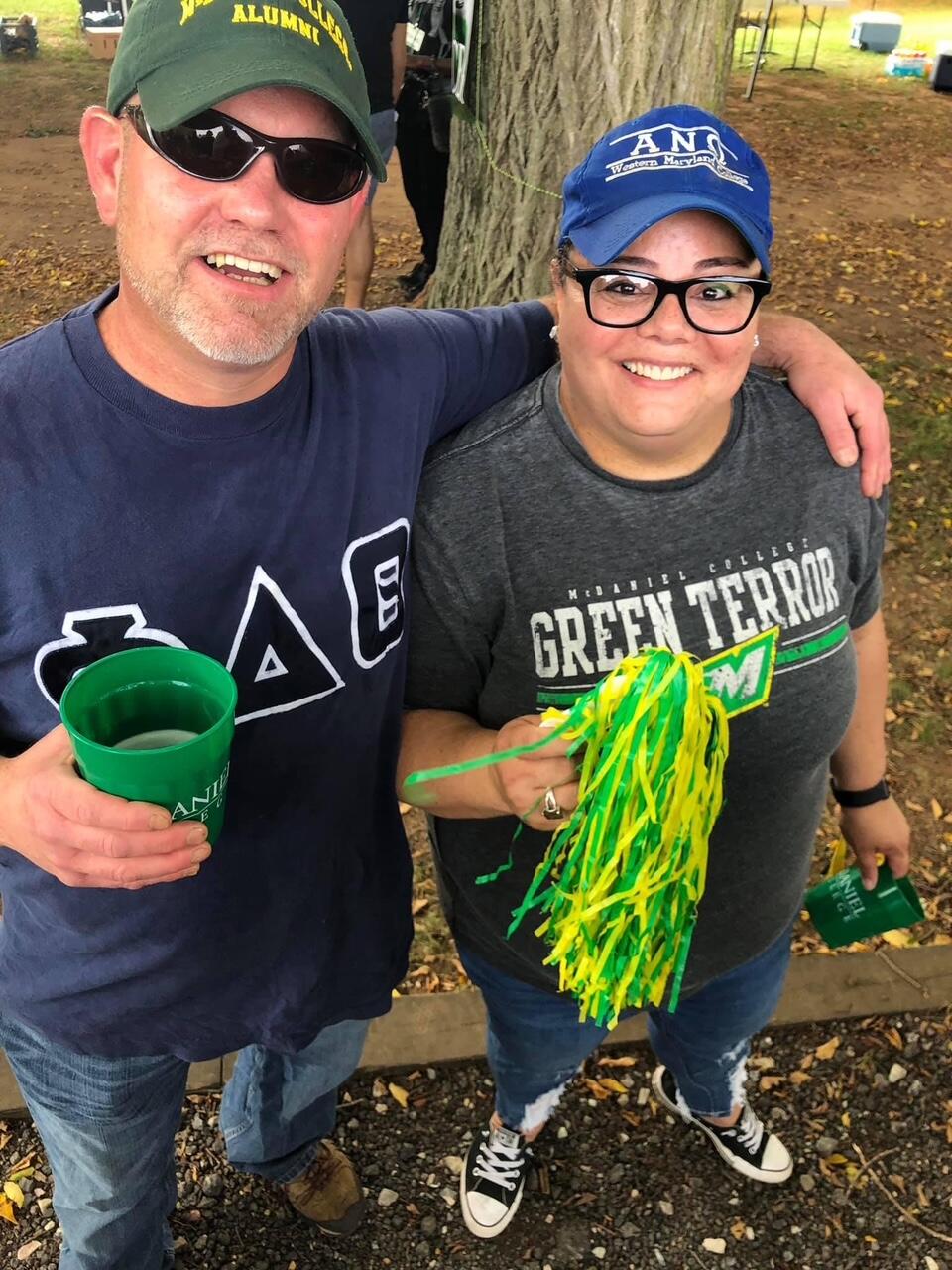 Pete and Marcie Mason stand outside wearing McDaniel shirts and holding a pompom.