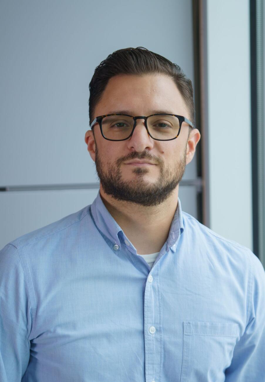Headshot of Christopher Palmore wearing a blue button-up shirt and black-rimmed glasses.