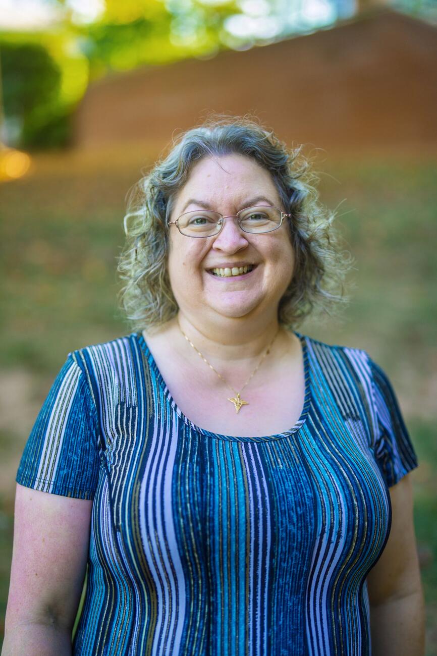 Laura Steakin smiles while standing outside and wearing a blue striped shirt.