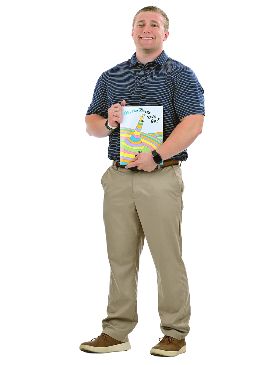 A male student stands holding a book.