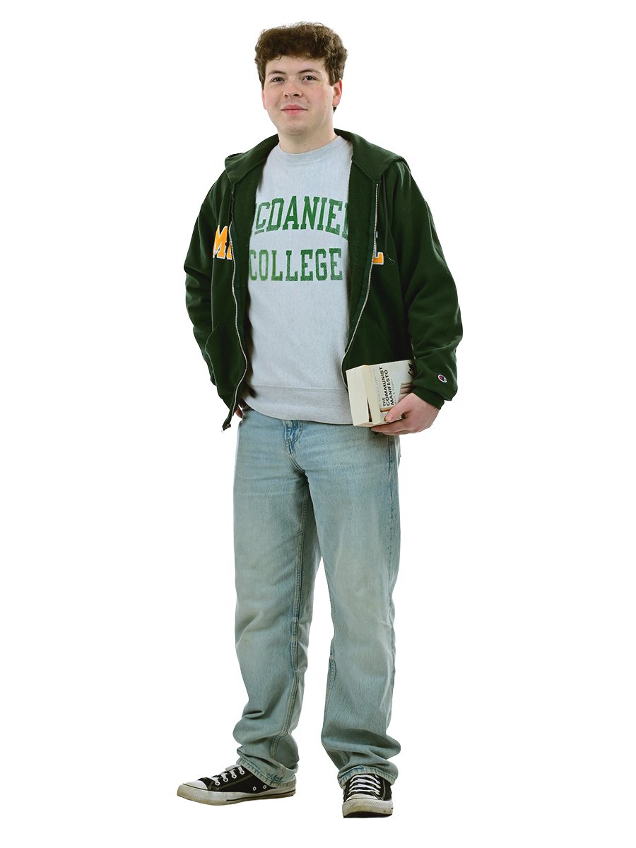 A male student in a McDaniel College shirt stands holding a book.