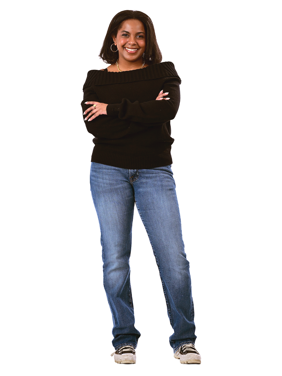 A female student in a black sweater and jeans stands with her arms crossed.