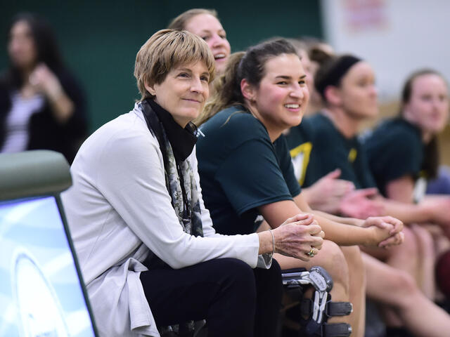 Coach Becky Martin sitting with basketball players on the sidelines.