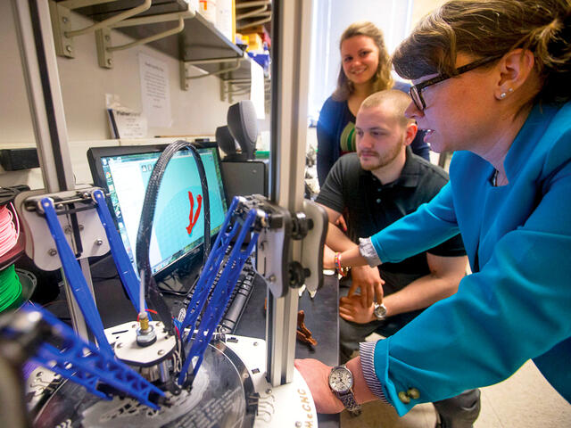 Biology professor guiding students in 3D printing.