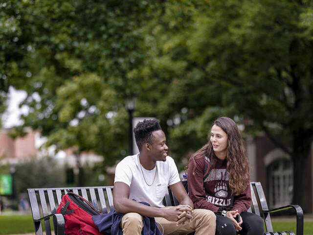 Students in conversation sitting on outdoor bench.