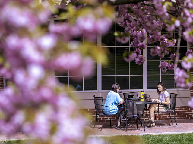 Two students in conversation sitting at outdoor table.