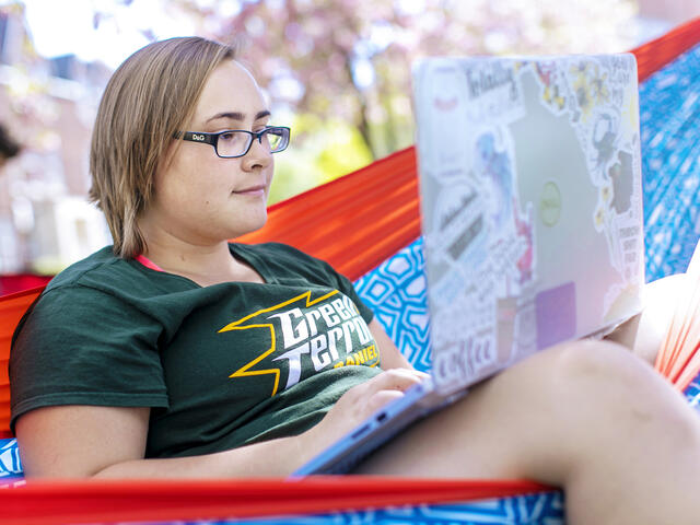 Student on computer in hammock on campus.