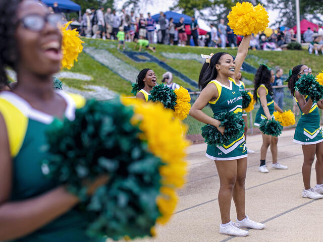 Cheerleaders cheering on team at homecoming football game.