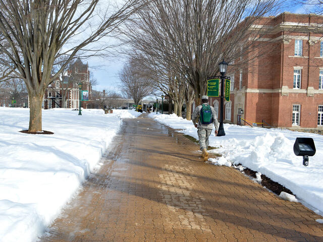 Student walking across campus sidewalks in the snow.
