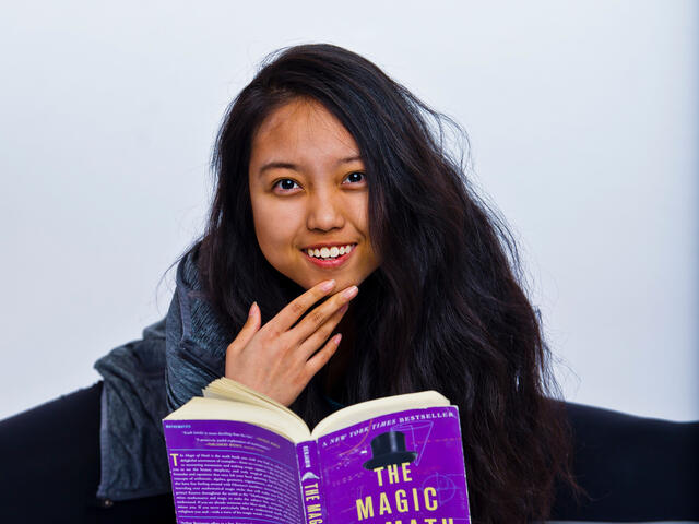 Angel Tuong holding a book while doing a split.