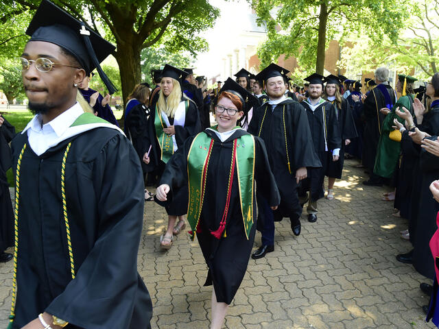 Graduates in cap and gown walking across campus.