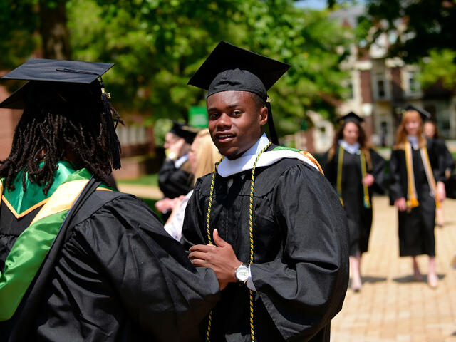 Graduates in cap and gown walking across campus.