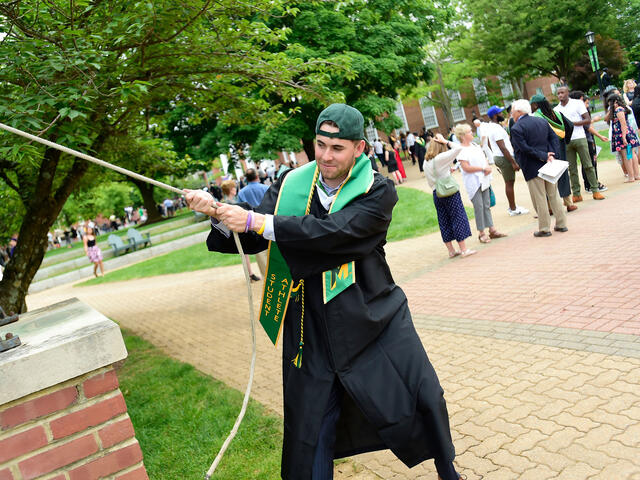 Graduate in cap and gown ringing the Bell.