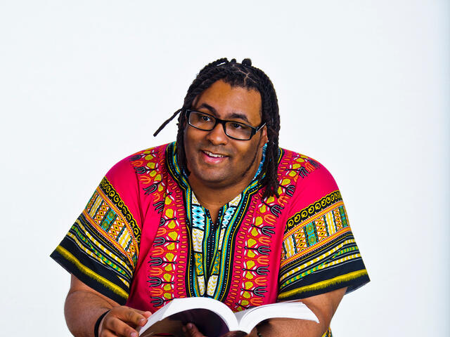 Wayne Young leaning on table flipping through pages of a book in front of a white background.