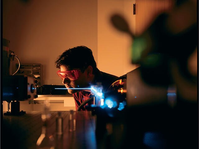 Student wearing goggles in a dark lab using lasers.