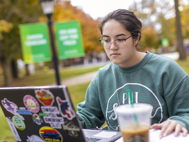 Student sitting at outdoor table and looking at laptop.