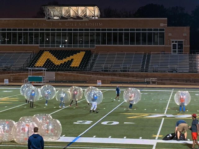 Ten students wear large inflated balls while playing Bubble Soccer on the Gill Stadium football field. 