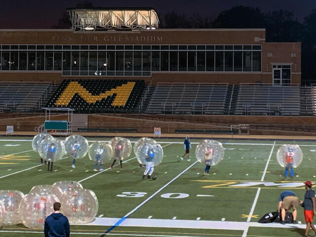 Ten students wear large inflated balls while playing Bubble Soccer on the Gill Stadium football field.
