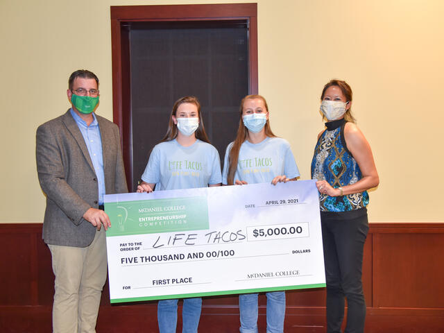 Four individuals hold up a large check