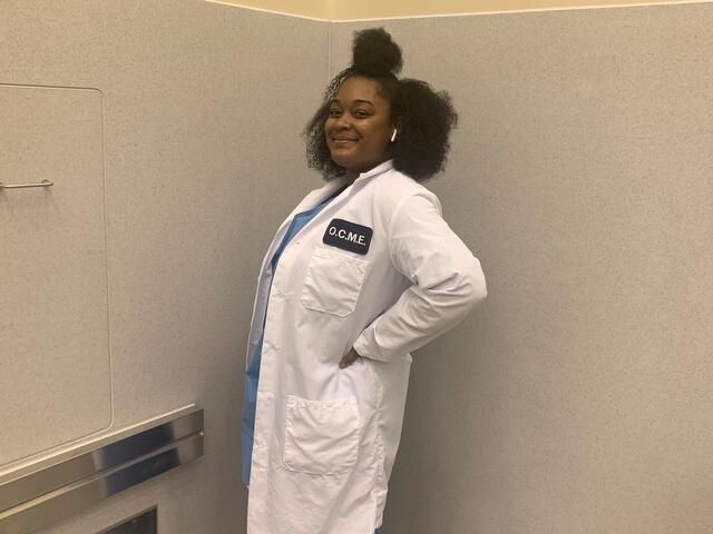 Alumni Treyana Johnson standing in her OCME lab coat.