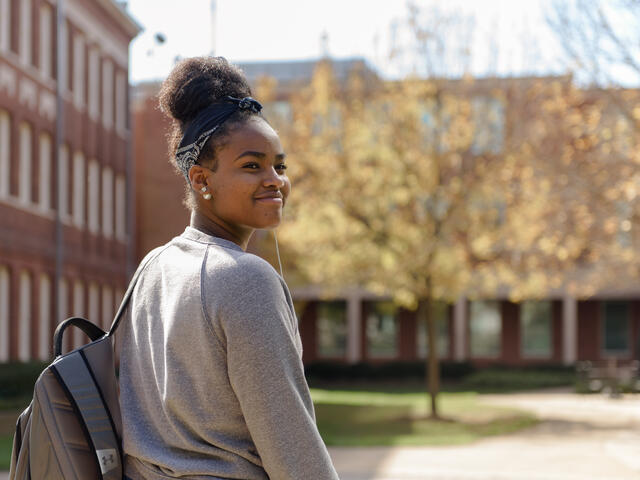 A student on campus looks back over her shoulder while smiling.