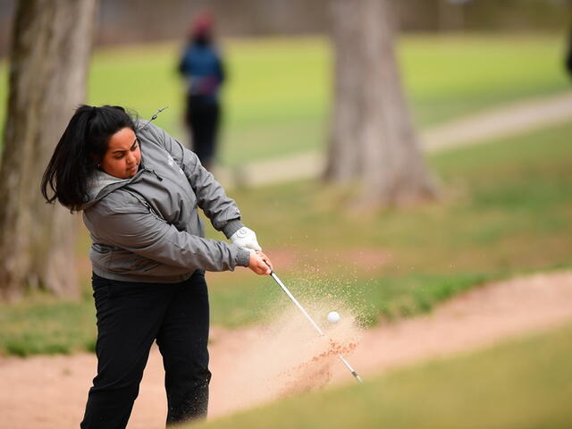 Photo of a student hitting a golf ball and kicking up dirt.