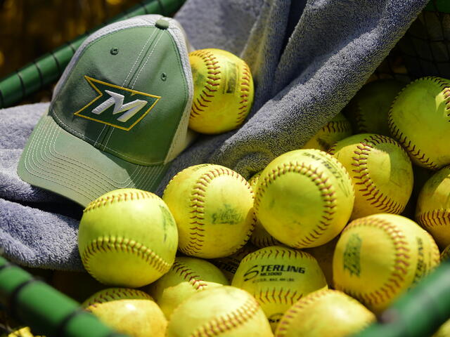 Photo of a green McDaniel hat with an M on the front on top of a towel and bright yellow softballs.