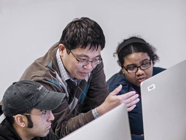 Photo of professor Paul Lin speaking with students at a computer.