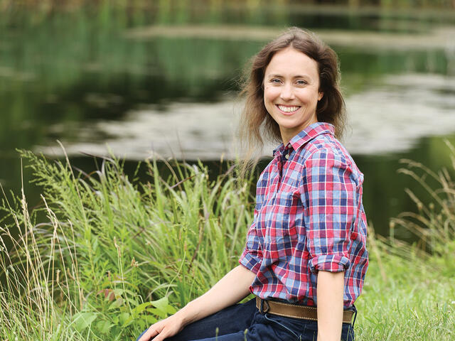 Photo of professor Margaret Christie sitting on the bank of a lake. 