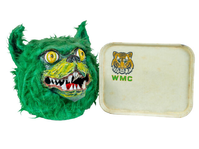 The head of the 90s Green Terror mascot head is displayed next to a WMC dining tray.