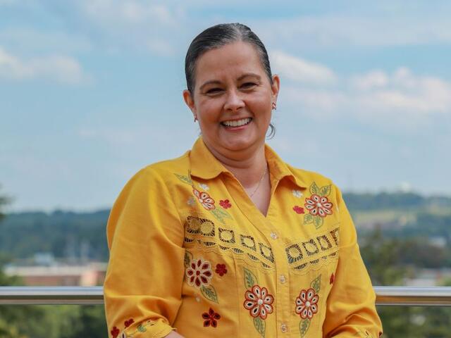 Photo of a woman standing on an overlook wearing a yellow flowered shirt with horizon behind her.