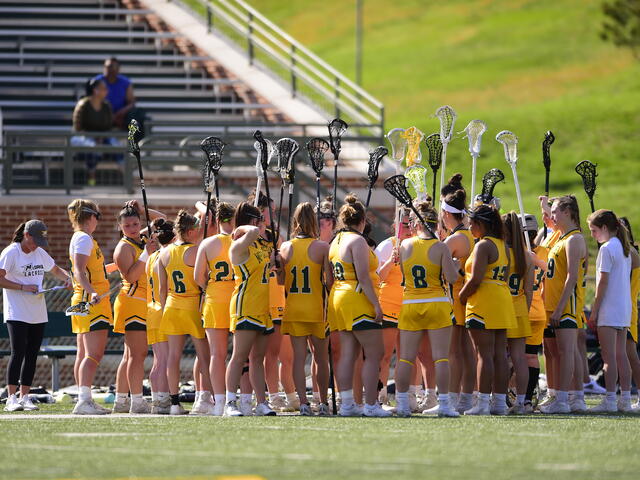 Women's Lacrosse huddle with lacrosse sticks in air
