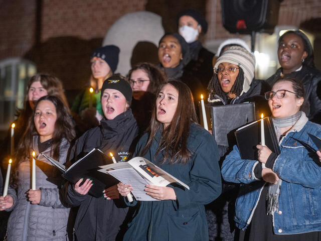 Students holding sheet music sing outdoors.