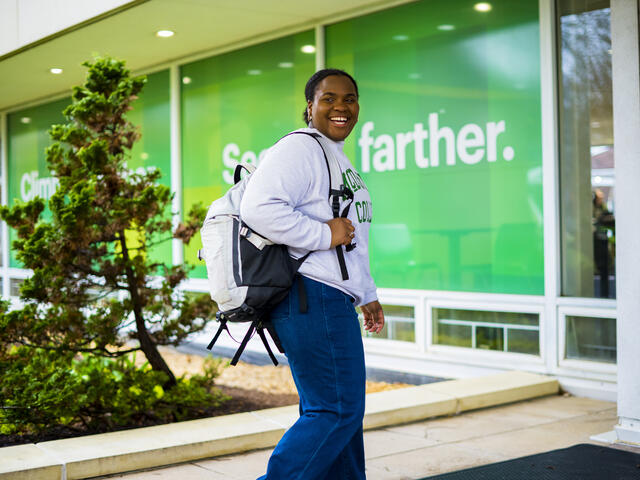 A student smiles to the side while walking with a backpack on their shoulder.