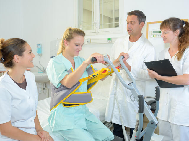 Four people in a hospital setting wearing medical scrubs, with one in a seated support brace.