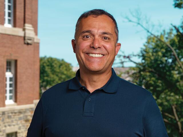 Photo of Adriano Lime e Silva in a blue button up smiling outside on campus.