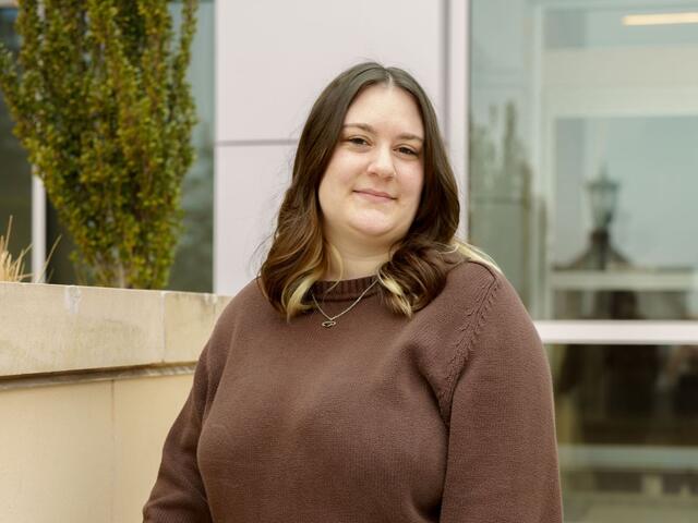 Portrait photo of Ashleigh Lobbins standing outside wearing a brown sweater.
